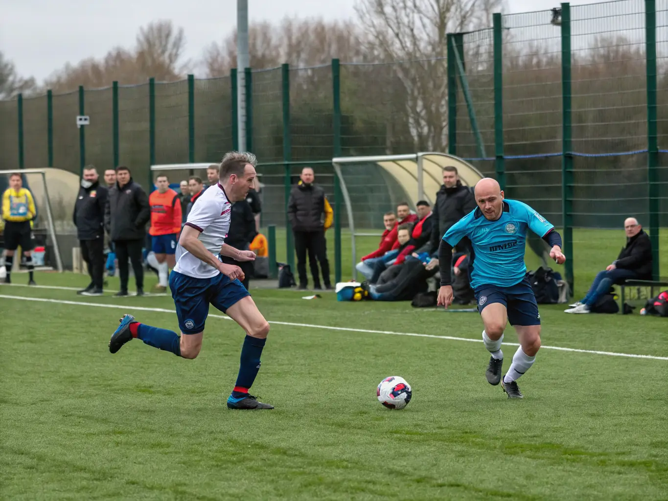 An action shot of adult players competing in a recreational football league match at FCBO FCB LES OLIVES, highlighting the competitive spirit and camaraderie.